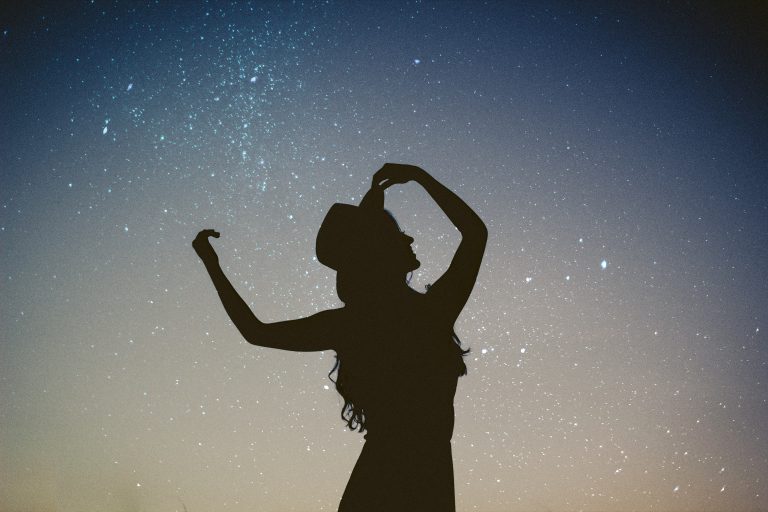 silhouette of woman holding hat in blue and gray nebula